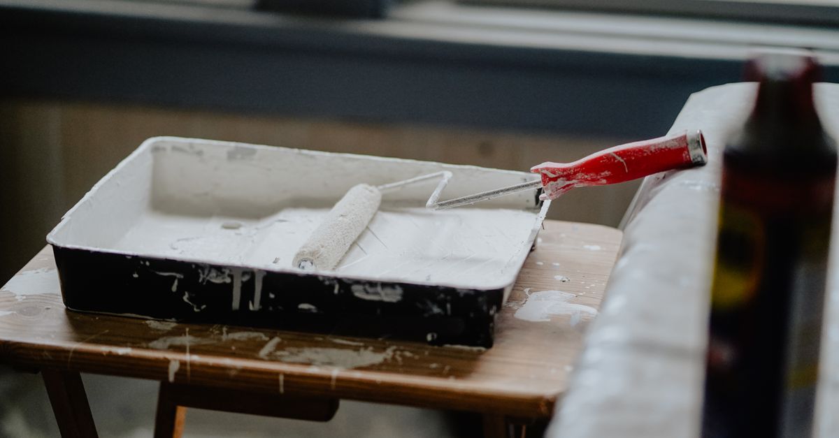 A paint roller and tray with white paint on a wooden table, indicating a renovation work.